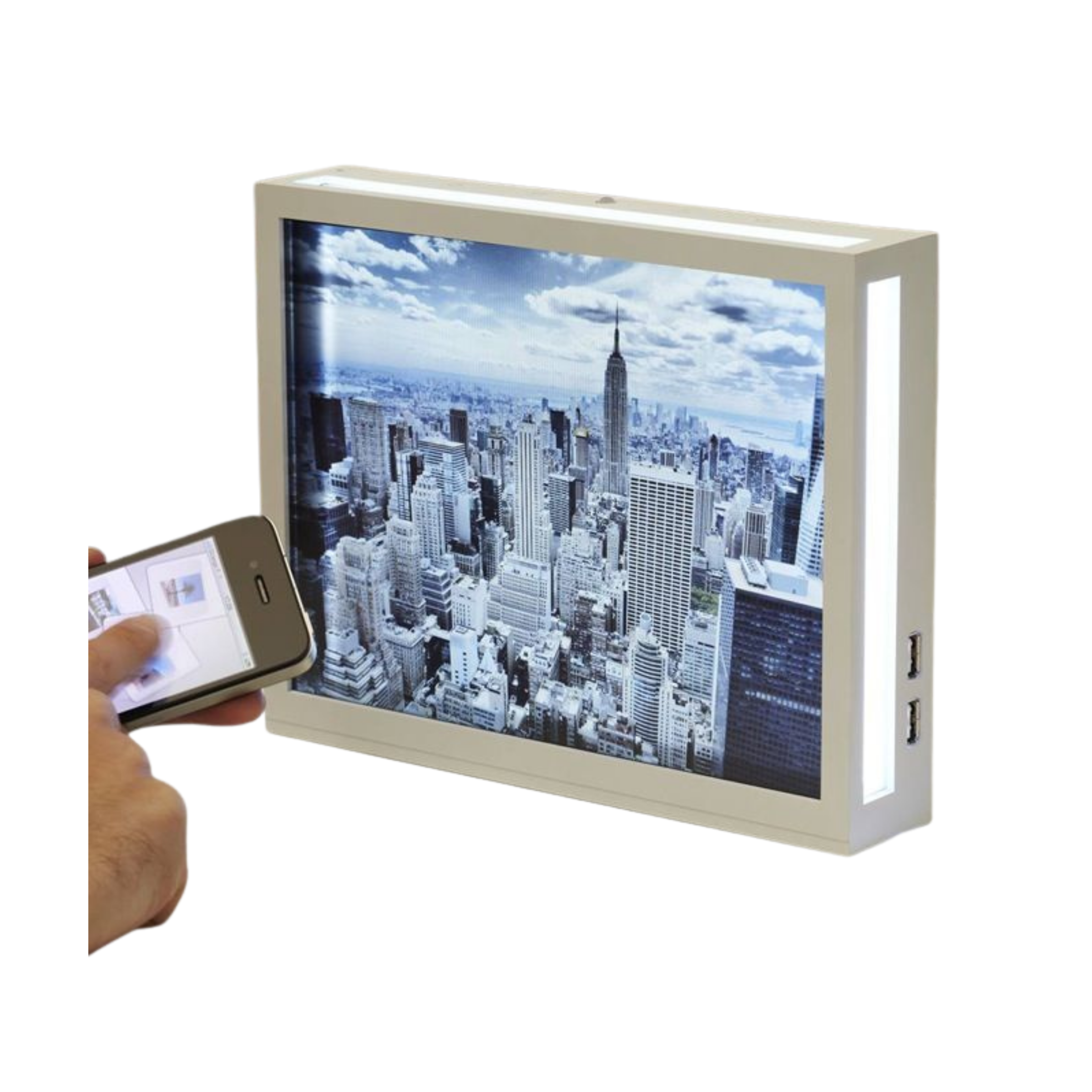 Boxy white connected photo frame showing a New York skyline, with a hand holding a phone controlling it