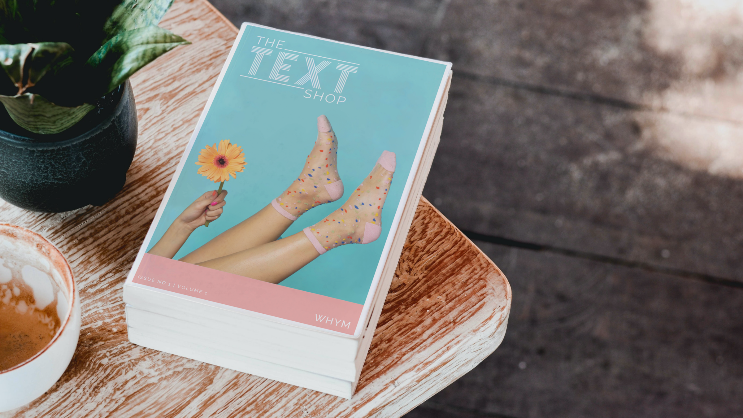 Printed zine on a wood table titled 'The Text Shop', cover showing legs in sheer socks and a hand holding a gerbera daisy