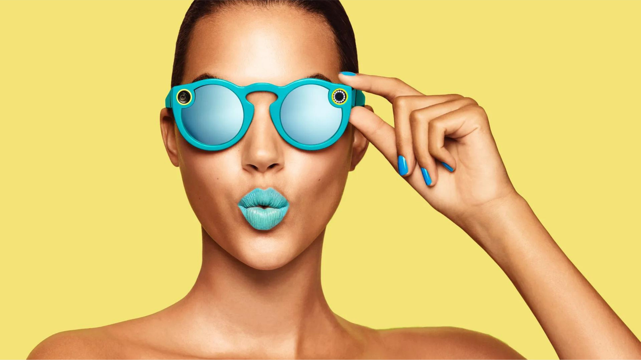 Model wearing teal Snap Spectacles camera sunglasses against a yellow backdrop, with matching teal lipstick