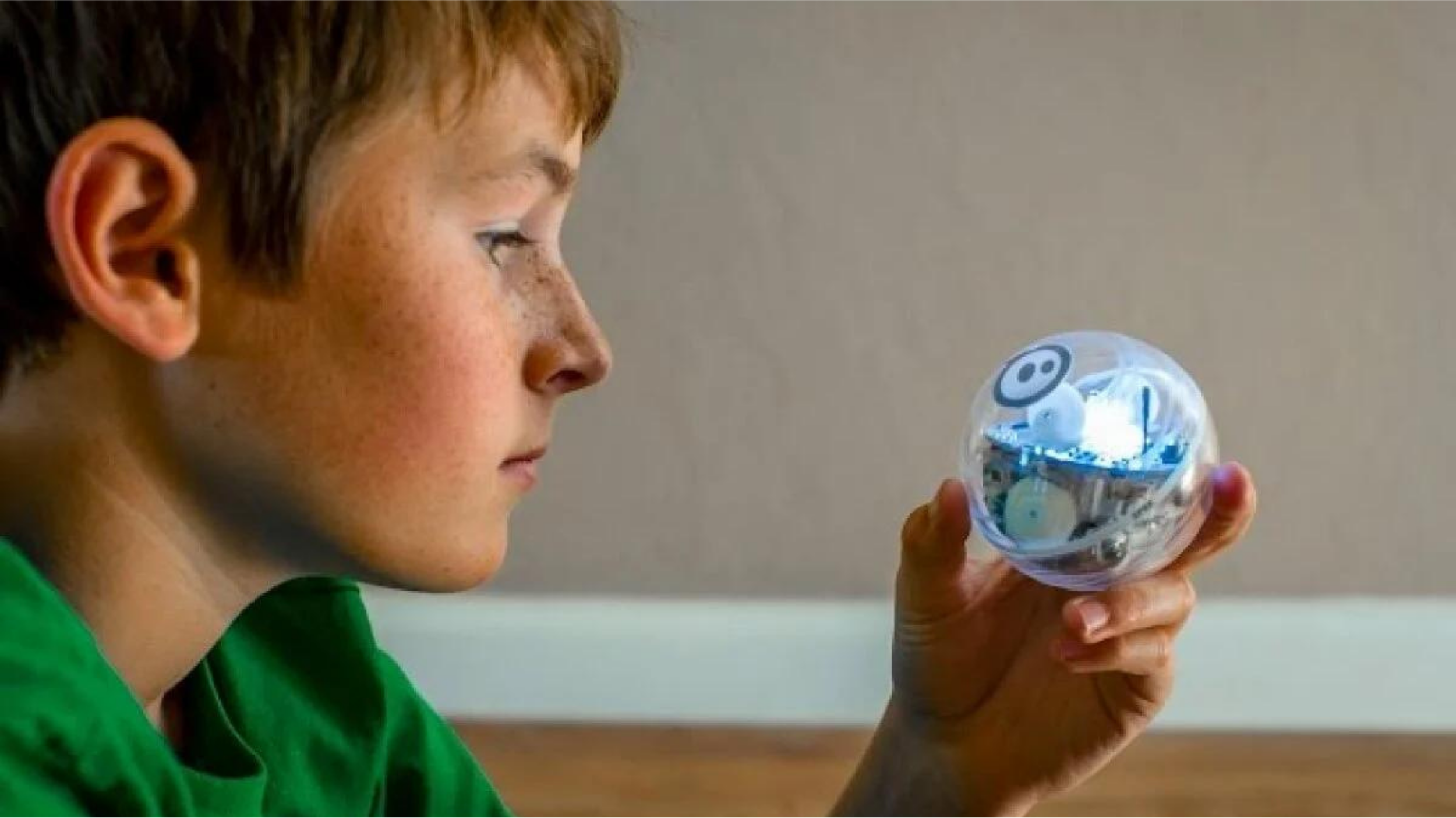 Boy in a green shirt holding a clear Sphero SPRK+ robot ball with visible internal circuitry and blue LED